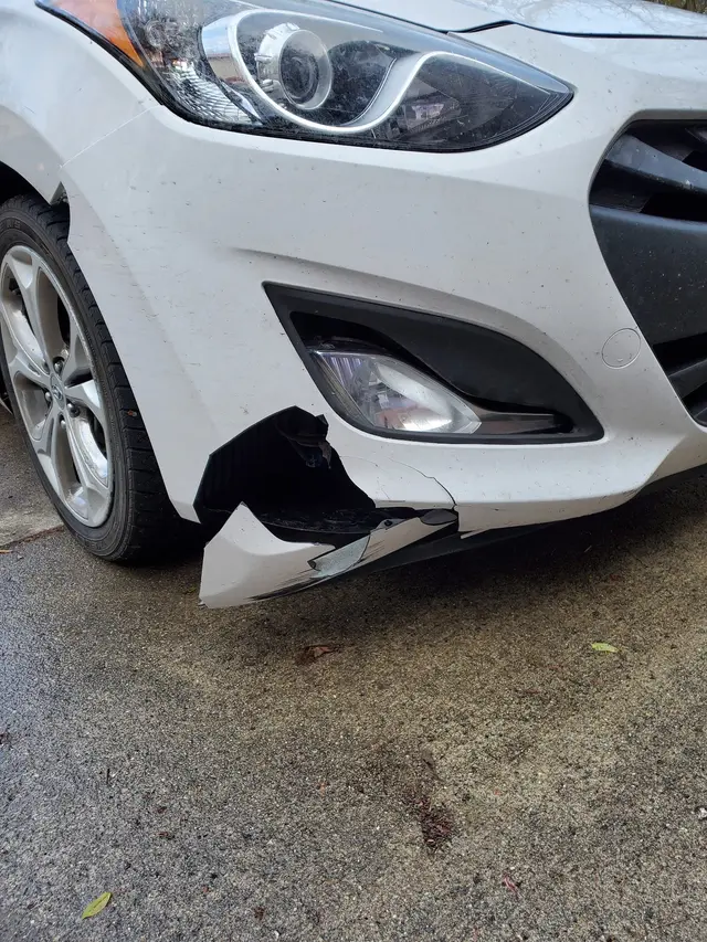 White hatchback with a torn front bumper cover