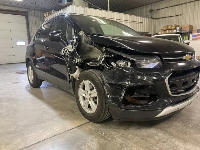 Black Chevrolet Trax with heavy front-end collision damage, in the shop before the repair